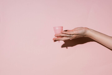Pink menstrual cup in female hands. Women's health, hygiene concept. Shadow of a hand on a pink...