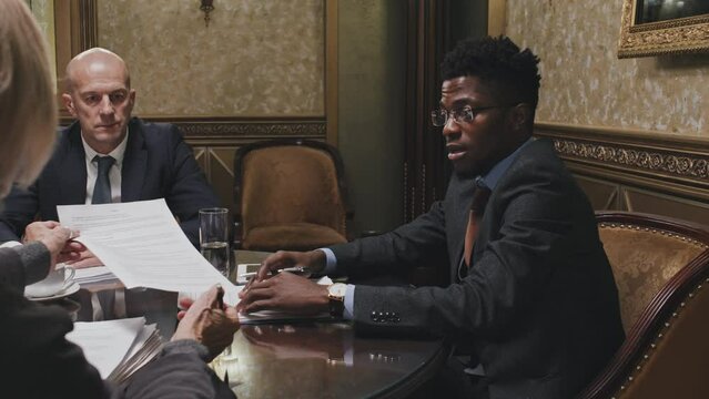 African American lawyer in formal suit sitting at meeting table in office and giving consultation about business contract to Caucasian clients