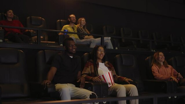 Mixed raced young couple sitting in movie theatre and watching film