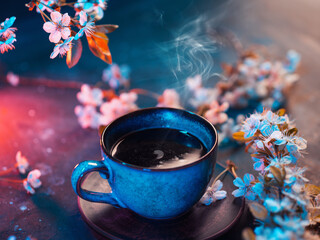 A cup of fragrant hot coffee on the table with a blooming cherry branch. Spring greeting card. Color backlight