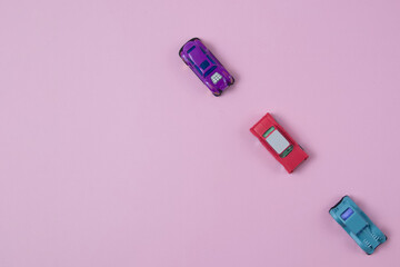 Cars of different colors go one after the other on a pink background with copy space. Minimalistic flat lay scene.