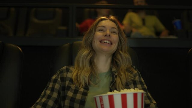 Cheerful woman watching a comedy movie at the cinema, eating popcorn