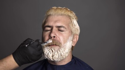 Hairdresser colorist dyes the mustache hair of a bearded man. Hair salon, hair coloring man. Attractive senior barber doing a haircut and haircolor for client at barber shop.
