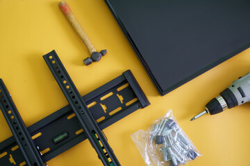 Bracket for wall mounting computer monitor or TV, electric drill-driver, mounting screws and TV screen on yellow background. Concept of wall mounting computer monitor or TV. Interior upgrade