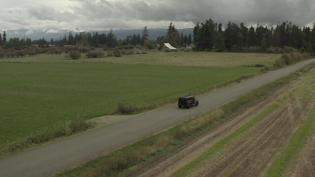 Drone actively following a red Jeep Wrangler on a country road in 4k