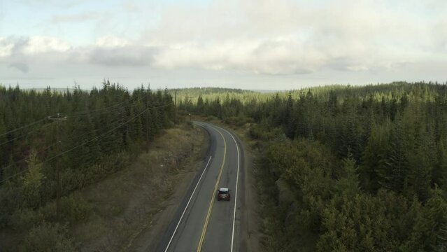 Drone shoot of a Grey Car driving on a road in the middle of a forest on a cloudy day in 4k