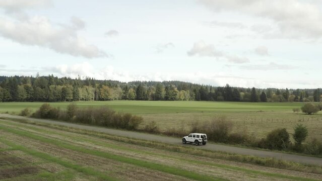 Drone actively following a White Jeep Wrangler on a country road in 4k