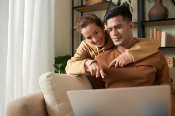 Young happy woman pointing at laptop and choosing the things online together with her boyfriend during their online shopping