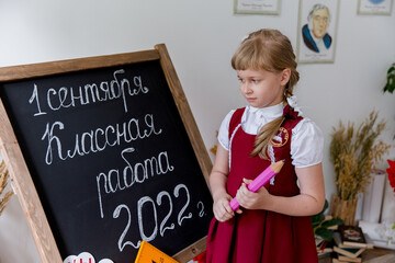schoolgirl stands near the blackboard with a pencil