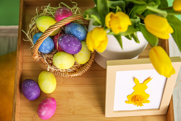 Basket with Easter eggs, photo frame and vase with tulips on table