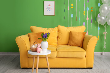 Flowers, basket of Easter eggs and rabbit on table in living room interior