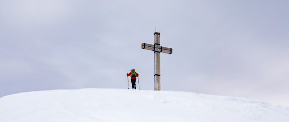 Panorama Bergsteiger auf einem Gipfelkreuz in den Alpen