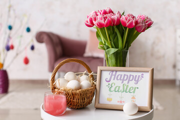 Basket of Easter eggs, candle, bouquet of tulips and photo frame with greeting card on table in room © Pixel-Shot