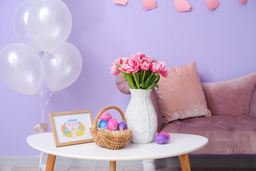 Basket with Easter eggs, tulips and photo frame on table in room