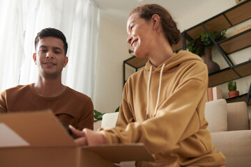 Young couple talking to each other and packing things together in the box sitting in the room