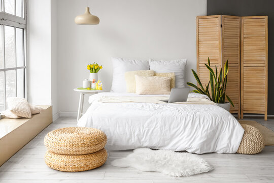 Comfortable bed with modern laptop, vase with tulips and Easter decor on table in bedroom interior