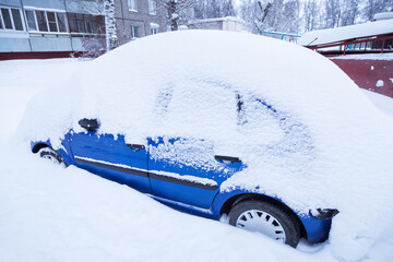 Blue car covered snow on winter town street after snowfall	