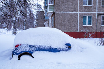 Blue car under snow parked on winter town street after heavy snowfall