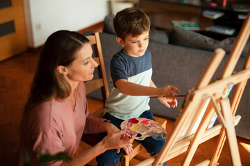 Mother and son painting at home. Little boy drawing with mom in living room.