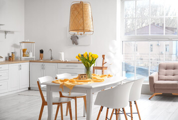 Cube calendar and vase with bouquet of tulips on dining table in kitchen interior. International Women's Day celebration