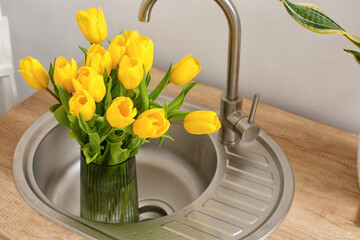 Vase with tulips in sink near light wall. International Women's Day celebration