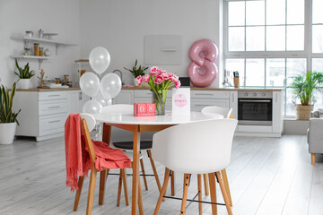 Greeting card with text HAPPY WOMEN'S DAY, cube calendar and flowers on dining table in kitchen interior