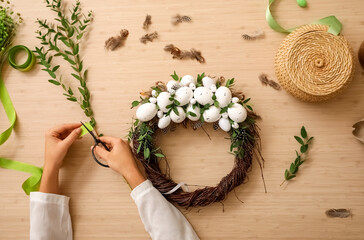 Woman making beautiful Easter wreath at table