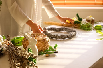 Woman making beautiful Easter wreath at table, closeup