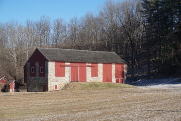 Obraz premium Stone Barn with Red Wooden Trim in Grassy Field on Sunny Winter Day