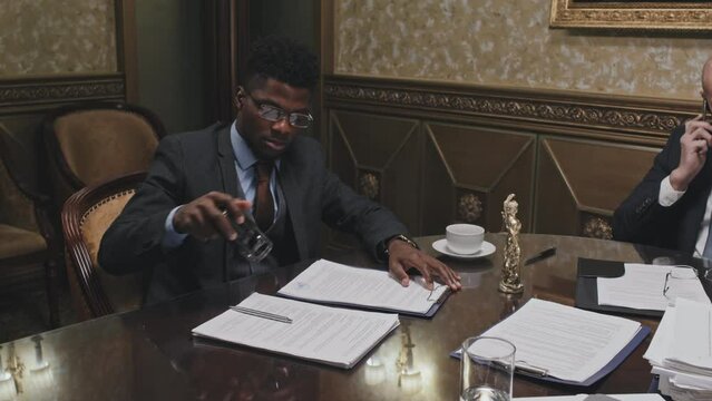 Zoom in shot of African American lawyer in formal suit signing and stamping document while working with colleagues in office
