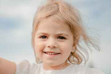 Closeup portrait of blonde little smiling caucasian girl. Looking at camera. Summertime. International children day