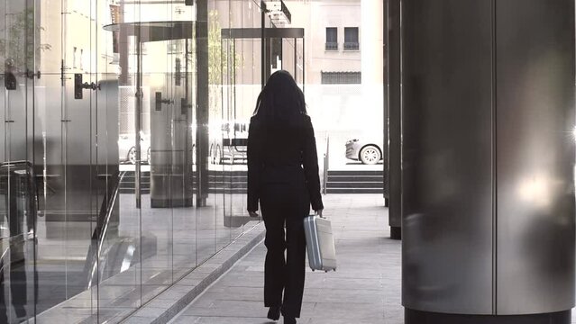 Young Asian business woman walking outside the office in the city centre carrying a silver briefcase. She is walking away from camera.