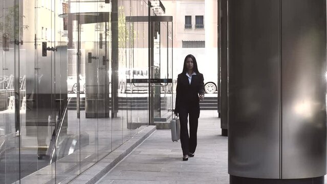 Young Asian business woman walking outside the office in the city centre carrying a silver briefcase. She is walking towards the camera.