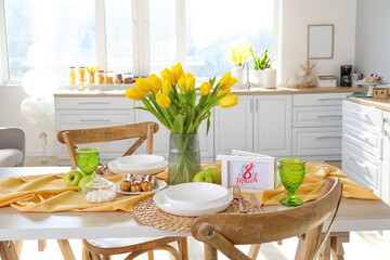 Dining table with setting and beautiful tulips in light kitchen. International Women's Day celebration