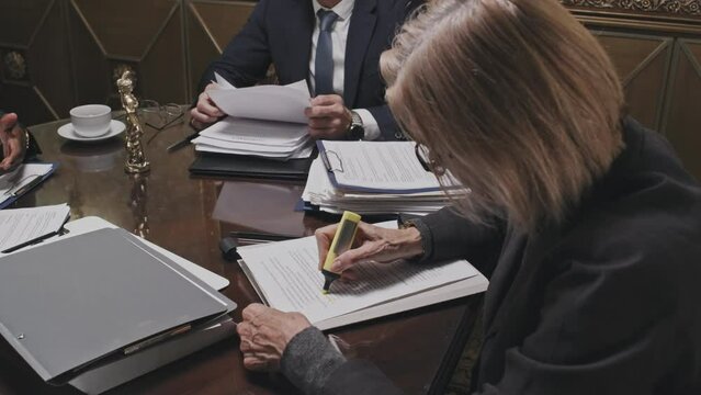 Female lawyer sitting at office table, reading document and marking text with highlighter pen