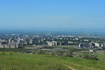 view of the city landscape in central asia in spring with pipes and with grass in the foreground and blue sky
