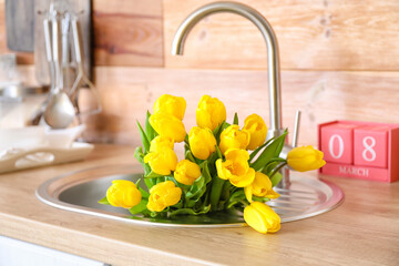 Bouquet of tulips in sink and cube calendar on kitchen counter near wooden wall. International Women's Day celebration