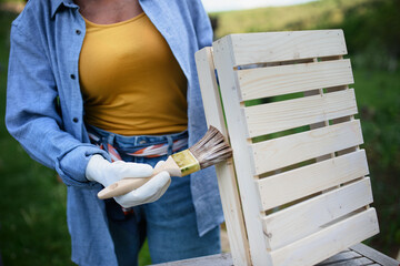 Close up of senior woman hand with paintbrush impregnating wooden crate outdoors in garden.