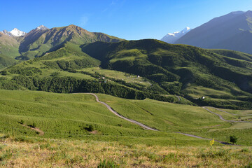 Fototapeta na wymiar green mountains with road, with snowy peaks in spring with blue sky in central asia kyrgyzstan