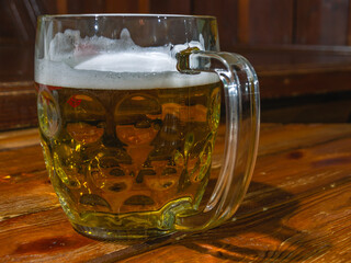 A large mug of beer stands on a dark wooden table. Beer with foam in a glass mug. An alcoholic...