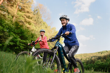 Low angle view of happy active senior women friends cycling together outdoors in nature.