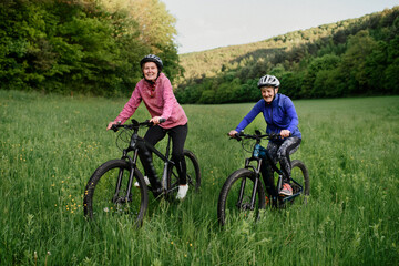 Fototapeta na wymiar Happy active senior women friends cycling together outdoors in nature.