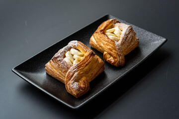 dessert is a small puff pastry pie with stuffing inside on a black serving plate on a black background . A piece of cake with a cut