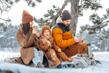Happy family with cups of hot tea spending time together in winter forest