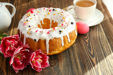 Tasty Easter cake with egg, flowers and cup of tea on wooden background