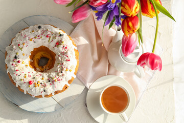 Tasty Easter cake, cup of tea and vase with flowers on light background