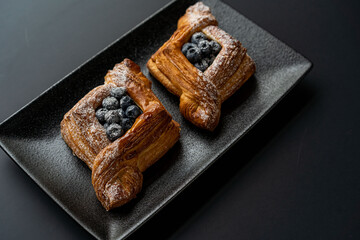 dessert is a small puff pastry pie with stuffing inside on a black serving plate on a black background . A piece of cake with a cut