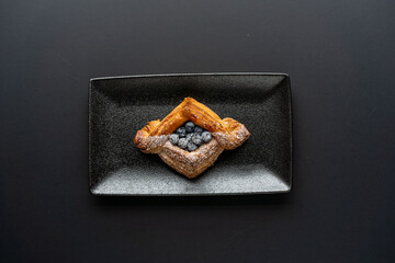 dessert is a small puff pastry pie with stuffing inside on a black serving plate on a black background . A piece of cake with a cut