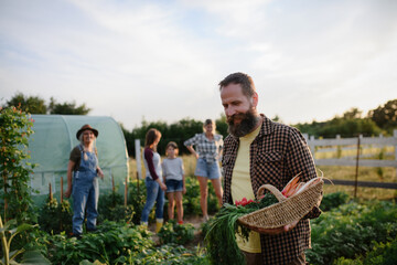 Happy mature man carrying crate with homegrown vegetables at community farm.