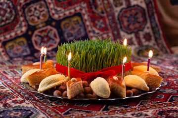 Beautiful Novruz tray on rug with semeni - wheat grass, pakhlava, shekerbura and festive candles on national Azerbaijani carpet table cloth. Spring equinox and new year celebration in Baku.